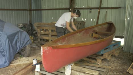 a young male carpenter cleans up after repairing a canoe