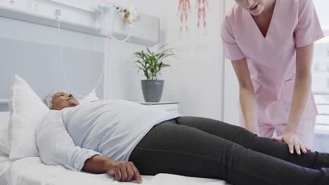 happy diverse female physiotherapist treating leg of senior female patient, slow motion