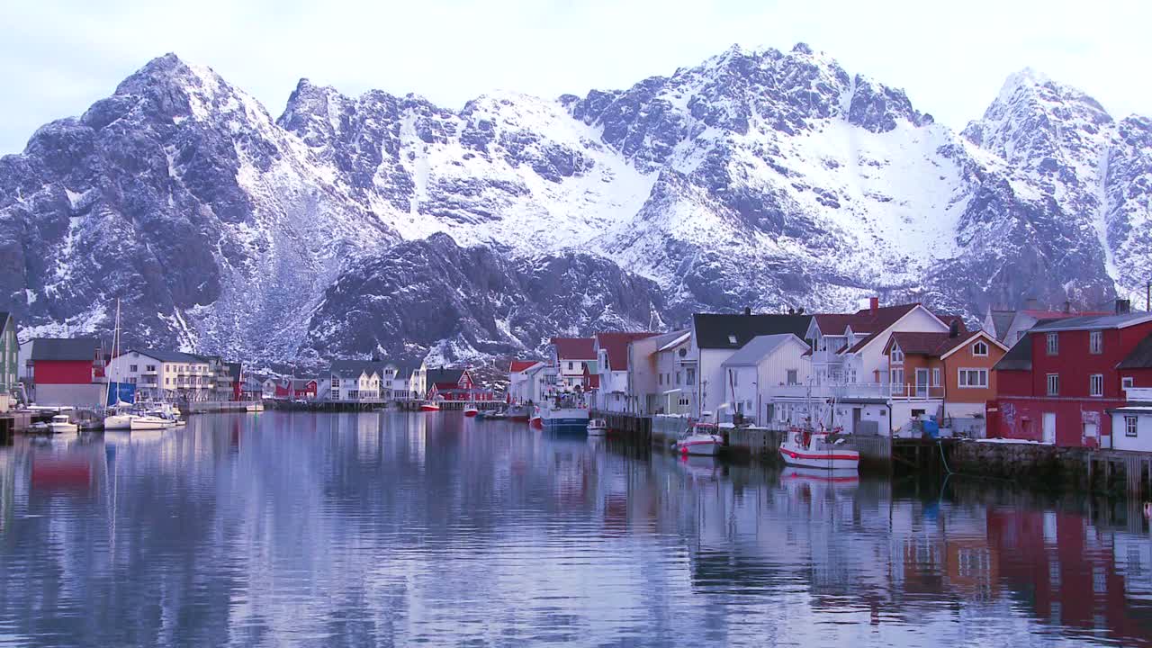 montañas cubiertas de nieve se reflejan en un puerto en un pequeño pueblo de pescadores en las islas árticas de lofoten noruega 1