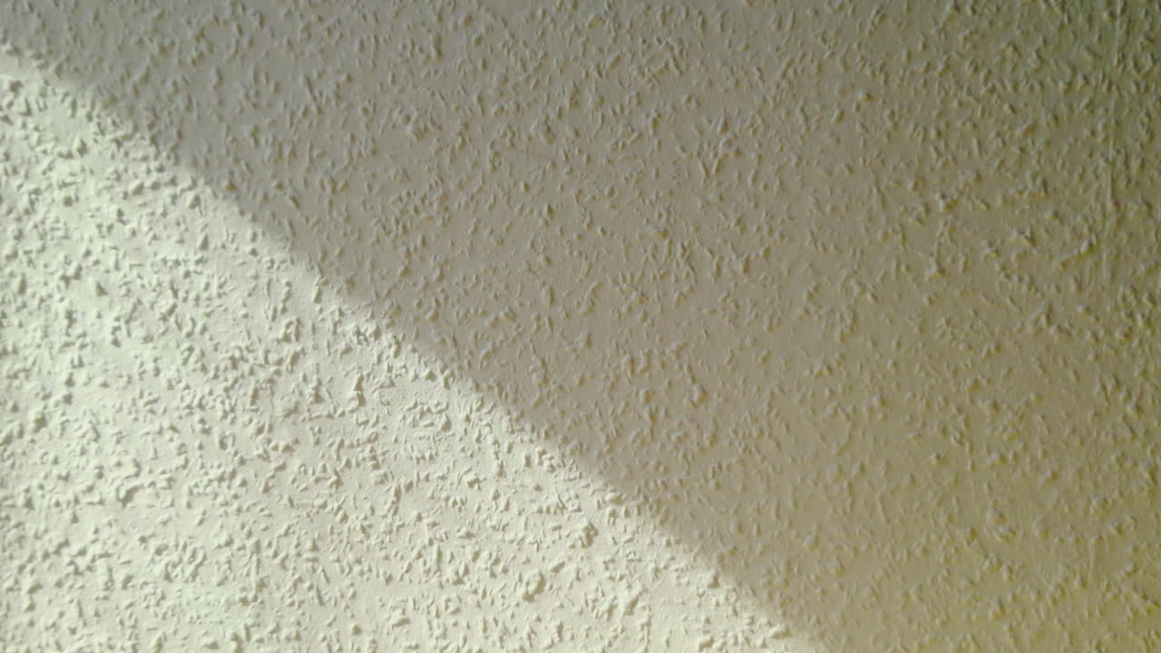 Soft sunlight casting a diagonal shadow across a textured wall surface. Minimal abstract scene highlighting plaster texture, light contrast and simple interior architecture detail