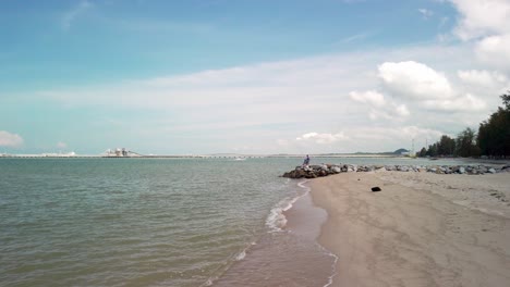 a drone-like low-to-high angle shot captures the coastal serenity of pantai puteri beach in melaka, malaysia, during the daytime