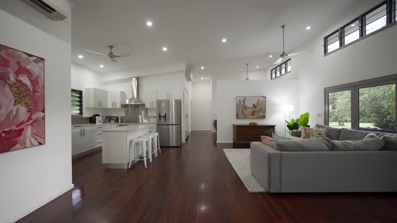 Open plan living room with wooden floorboards and white kitchen with stainless steel appliances