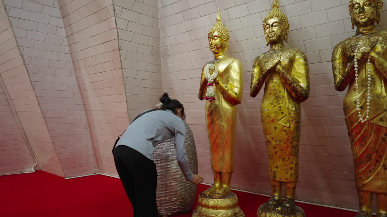 Woman worships golden Buddha statues in a temple