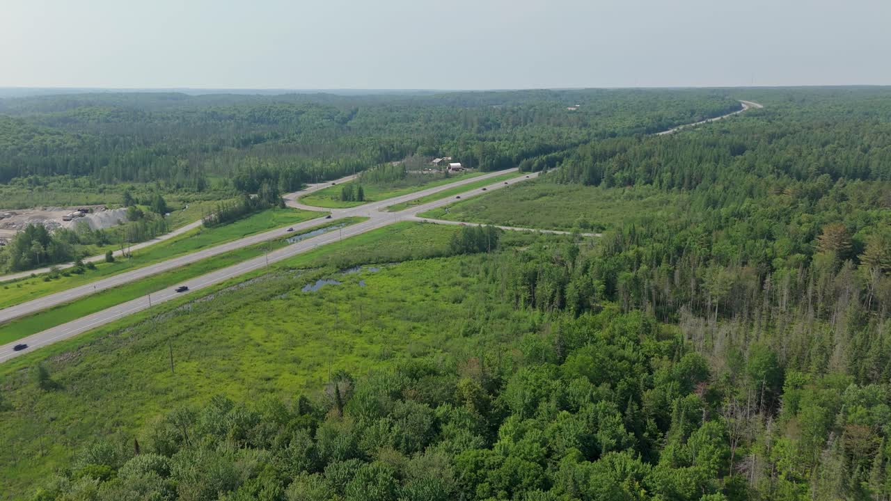 Aerial flyover of Muskoka rural landscape with forest, farm fields, and roads under clear sky