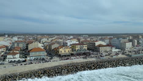 Olas-Rompiendo-En-El-Malecón-De-La-Playa-De-Furadouro-Con-Paseo-Marítimo-Y-Restaurantes-Junto-Al-Mar-En-Ovar,-Portugal