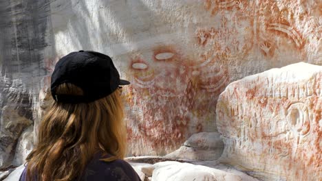 Una-Mujer-Observa-Las-Pinturas-Rupestres-Del-Arte-Rupestre-De-Bumeranes,-Manos,-Hachas-De-Piedra,-Escudos,-Redes-Y-Una-Variedad-De-Huellas-De-Animales.