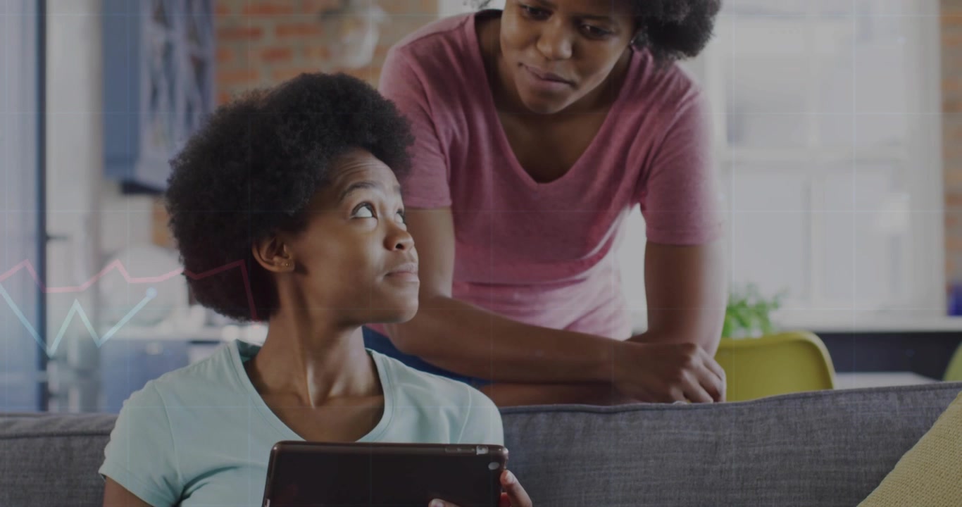 Adult woman approaching teen tapping tablet on couch, leaning over soothing teen for education help
