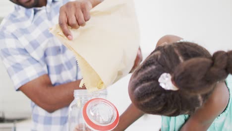 padre y hija afroamericanos felices llenando el frasco de almacenamiento con pasta, cámara lenta