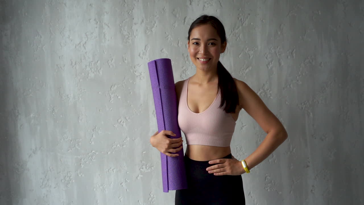 mujer influyente sosteniendo una alfombra de yoga, grabando un video tutorial para hacer ejercicio desde casa
