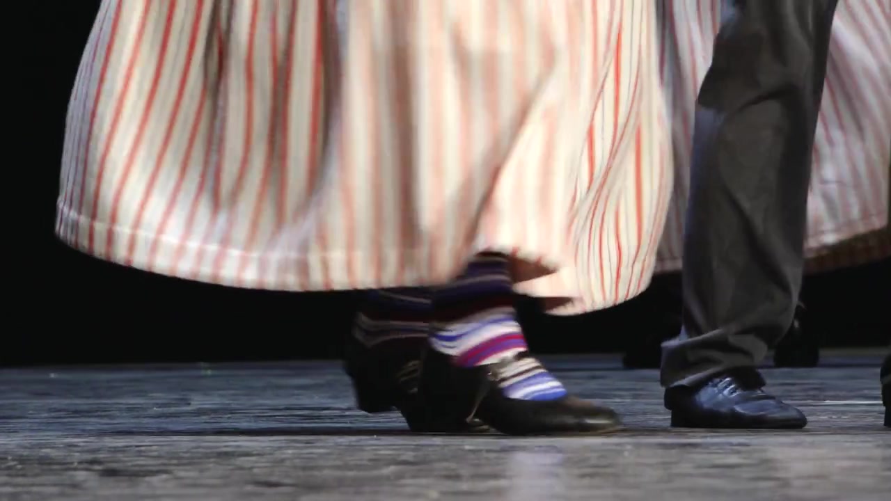 Primo piano dei piedi dei ballerini e delle gonne svolazzanti durante uno spettacolo folcloristico tradizionale sul palco, che mostra movimento, ritmo e dettagli dei costumi culturali