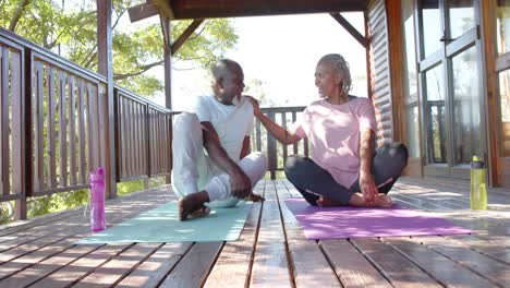 happy senior african american couple sitting on mats and talking on sunny terrace, slow motion