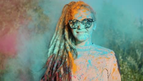 portrait of cute girl with dreadlocks smiling while friends are throwing gulal paint powder at her