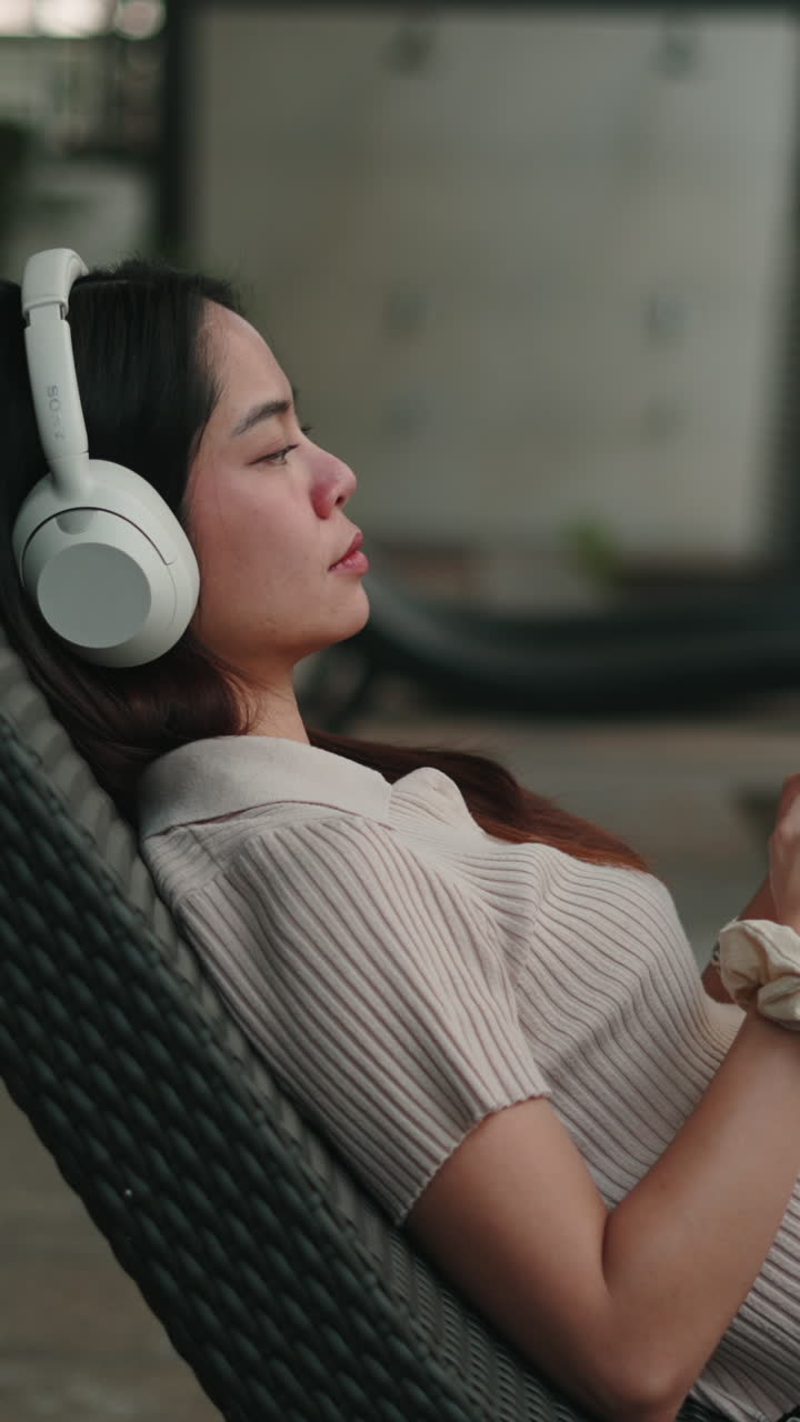 หญิงสาวชาวเอเชียกำลังผ่อนคลายและฟังเพลงด้วยหูฟัง