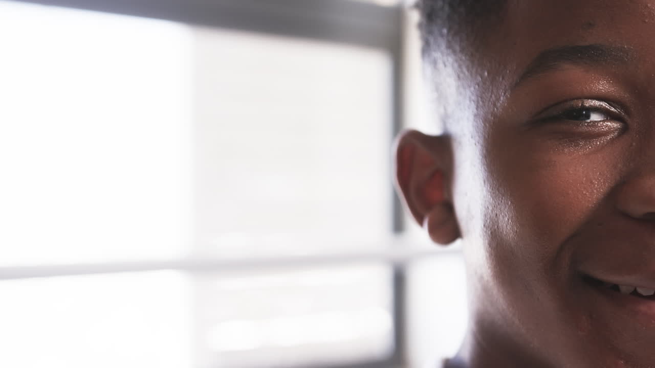 Smiling African American teenage boy in school, close-up of face with window in background, copy spa