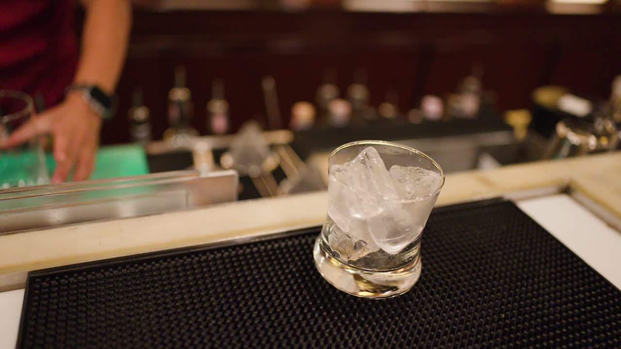 Bartender fills glass with ice on bar mat, warm lighting, shallow depth of field