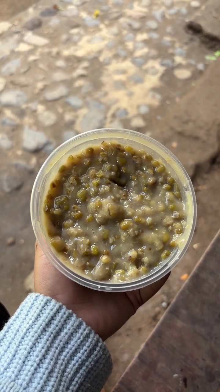 Elinde plastik bir kapta maş fasulyesi lapası tutan el.