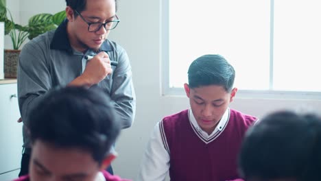 male teacher observes students diligently or supervising students who are taking exams in classroom