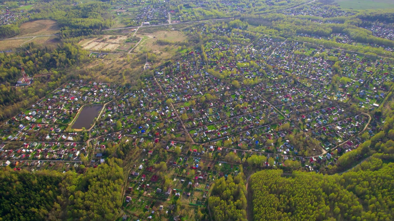Ampia vista con drone di un denso villaggio di campagna con stagni, strade tortuose, orti, margini di boschi e campi, utile per la pianificazione rurale, il settore immobiliare e l'uso del paesaggio campestre.