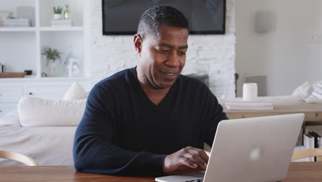 middle aged african american man sitting at a table using laptop computer at home, close up, zoom out