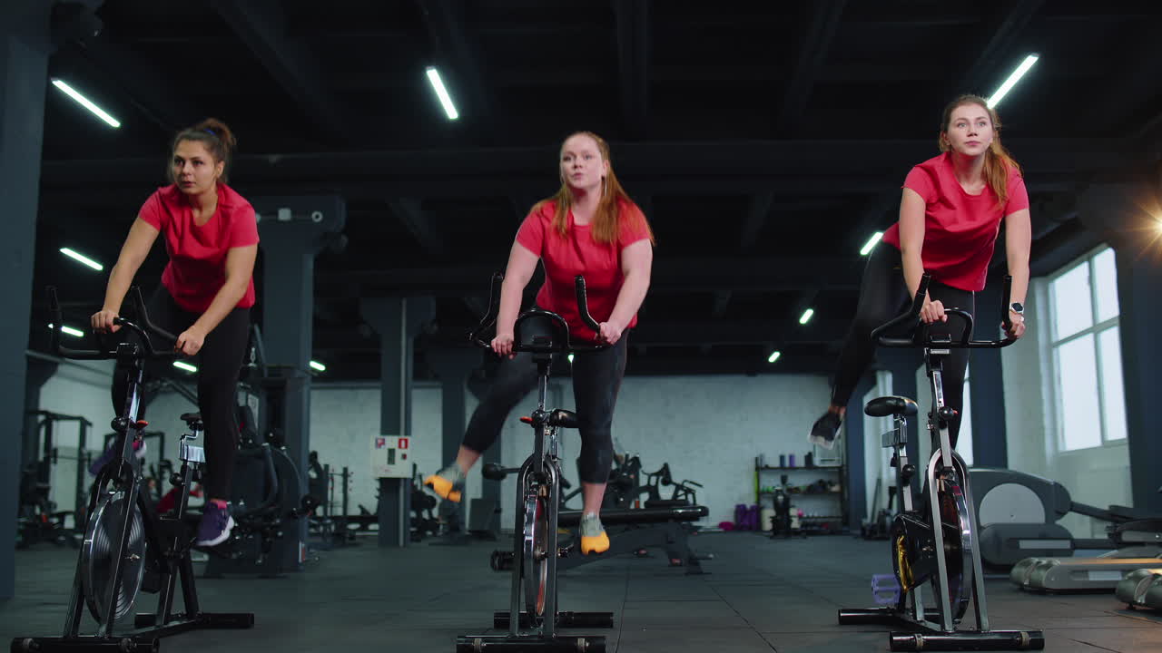 Gruppo di ragazze atletiche che eseguono esercizi di allenamento aerobico su una bicicletta stazionaria in palestra