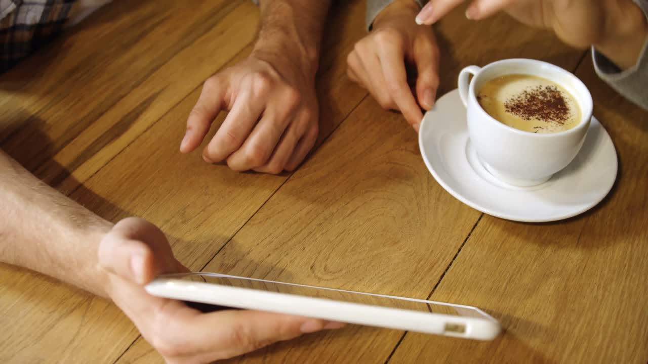 una pareja discutiendo sobre una tableta digital en un café 4k