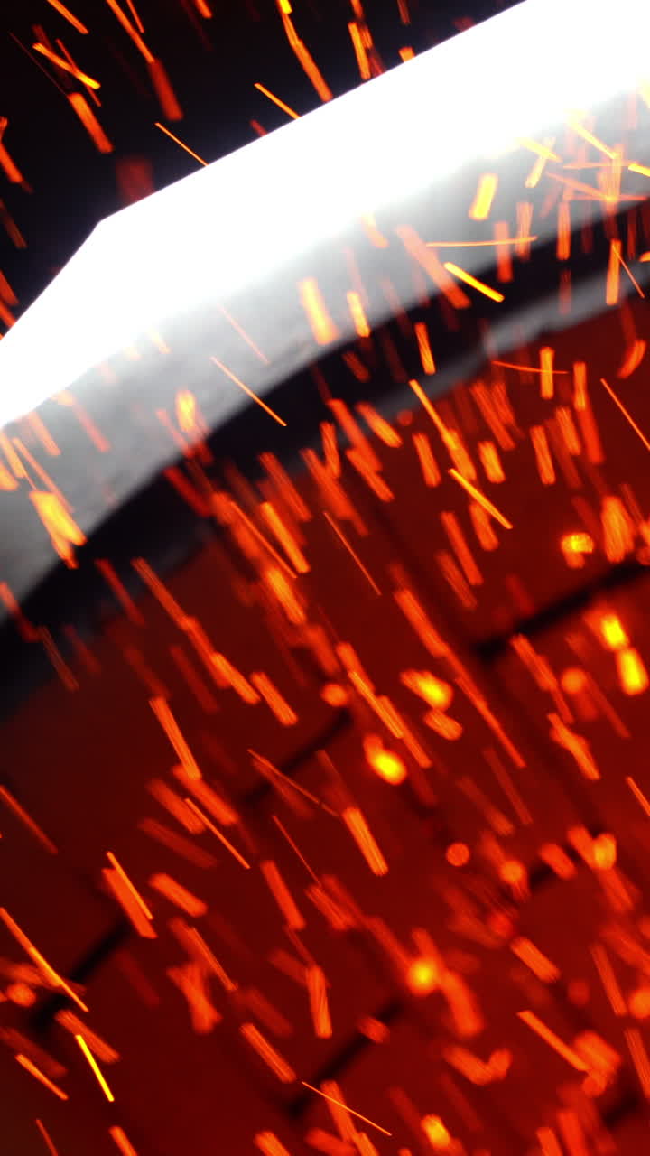 Numerous shining particles being emitted from a stove pipe. Orange and yellow sparks flying fast at black backdrop. Vertical video