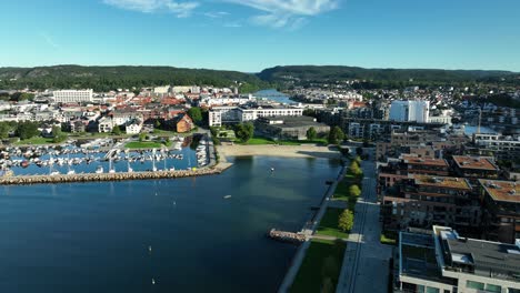 kristiansand in norway features modern residential structures, tangen ytterst alongside a marina filled with boats. green spaces and pathways invite outdoor activities under the bright blue sky