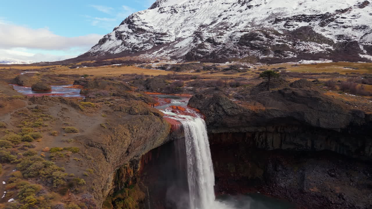 Aerial view of El Salto del Agrio waterfall in Caviahue, Neuquén, Argentina, with snowy andean mountains in background