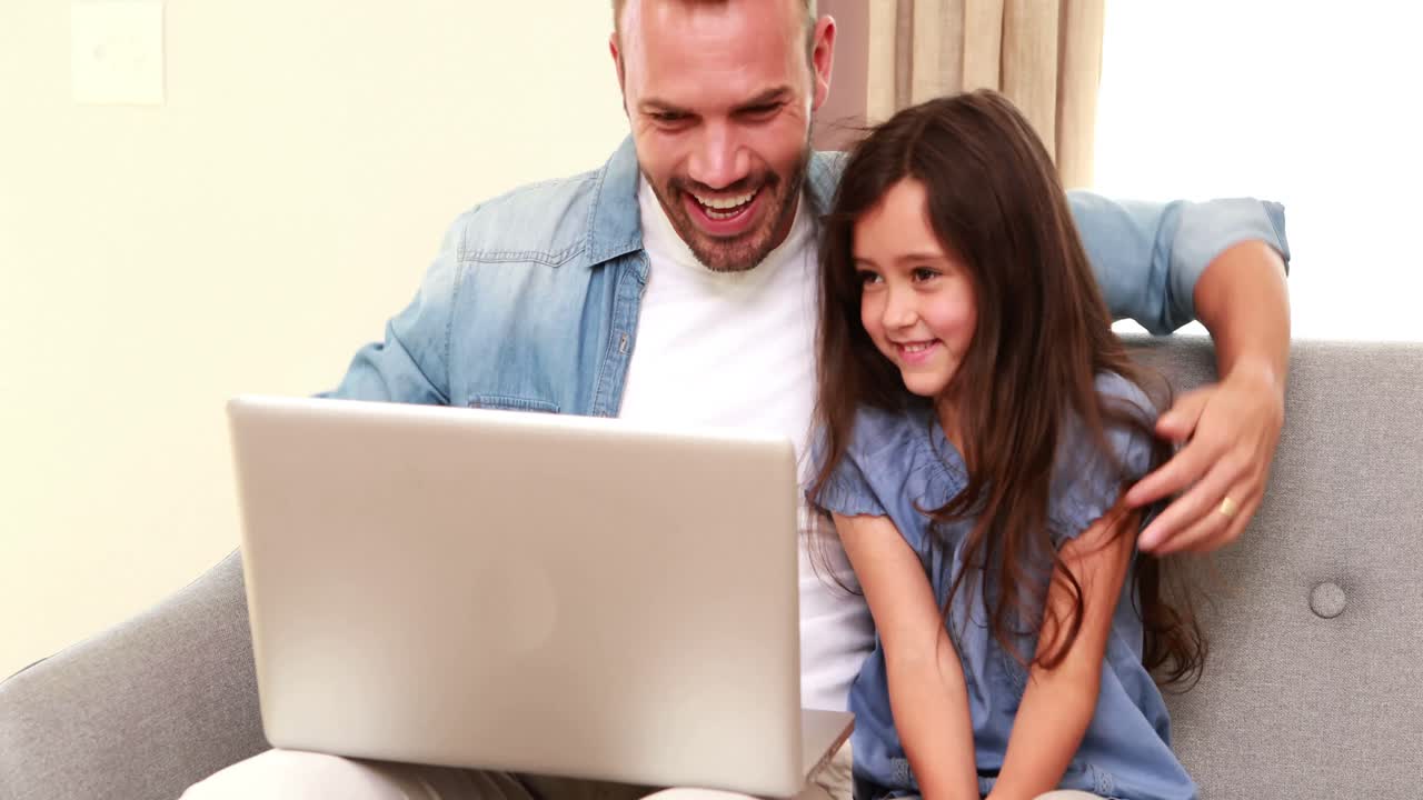 padre y hija felices usando computadora portátil