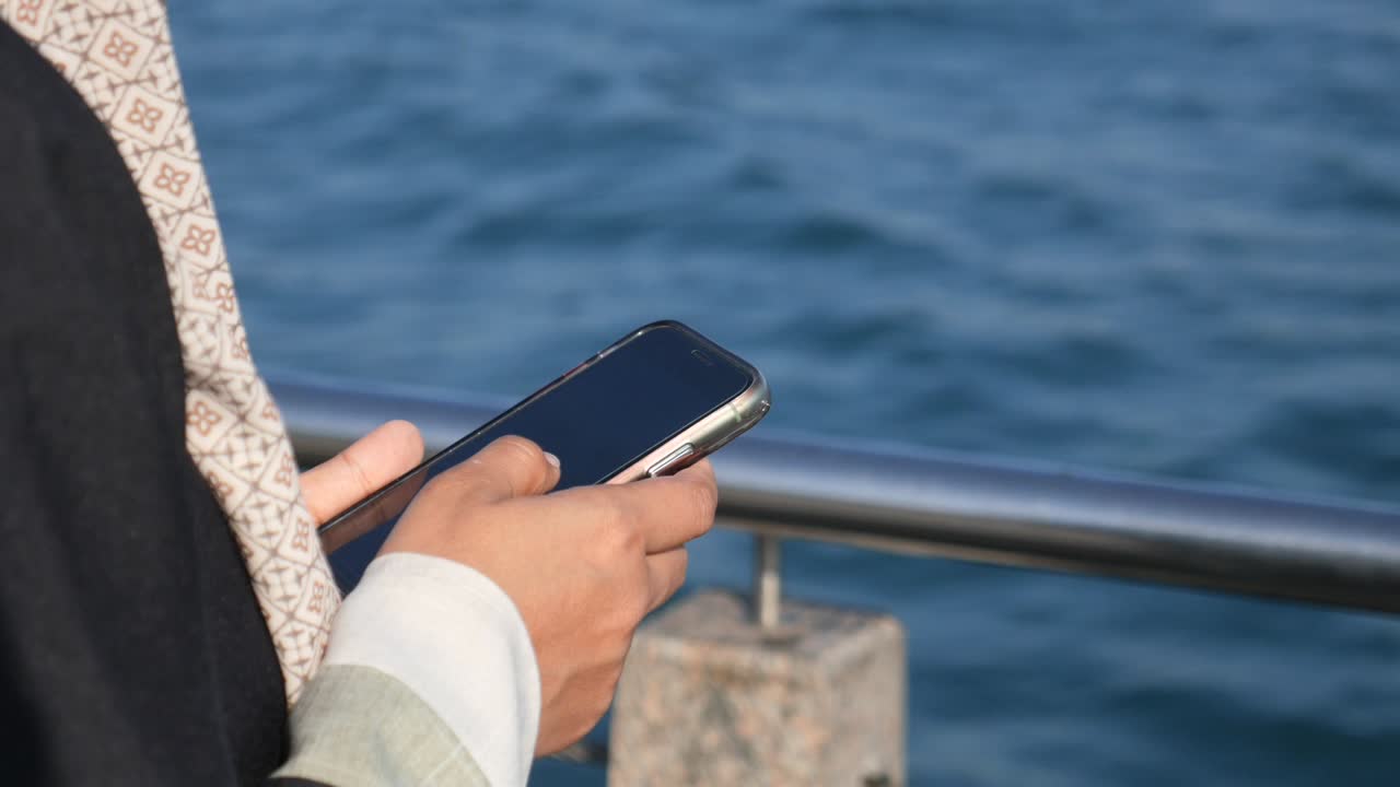 A person holding a phone by the ocean