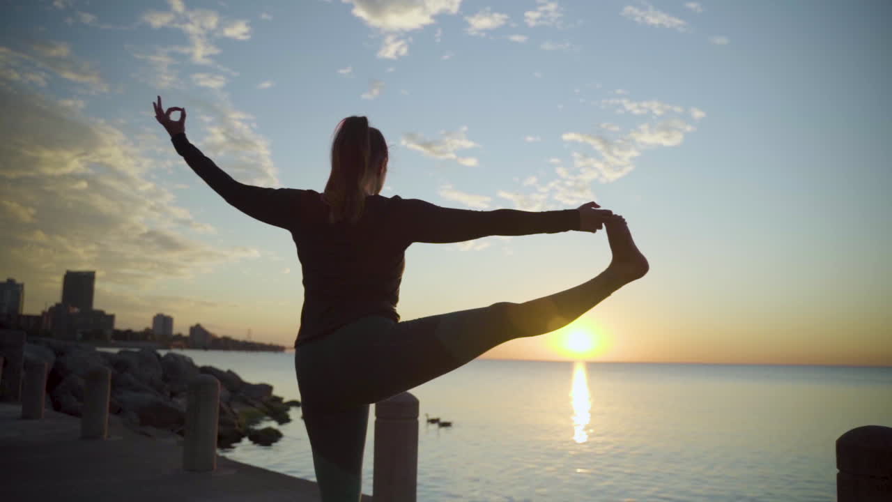 Silhouette of woman doing sunrise yoga near the water. Slow Motion.