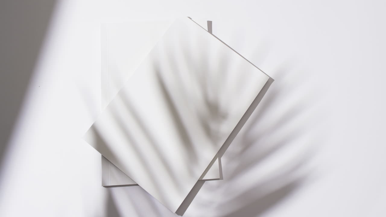 Video of shadow of plant over books with blank white pages and copy space on white background