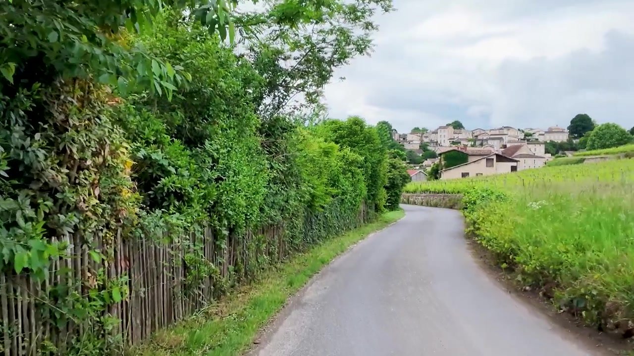 A smooth camera movement follows a winding rural road toward a historic French village
