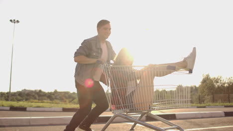 Un-Hombre-Corre-Y-Empuja-Un-Carrito-De-Supermercado-Haciendo-Rodar-A-Una-Chica-En-él,-Diversión-Loca-De-Los-Estudiantes