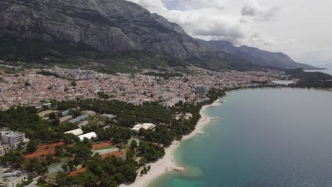 Coastal-Village-Makarska-In-Croatia-Surrounded-By-Beautiful-Ocean-And-Dramatic-Mountains,-Rising-Aerial-Shot