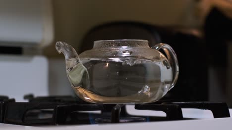 front side medium shot view of boiling water in a clear glass tea pot on a white stove