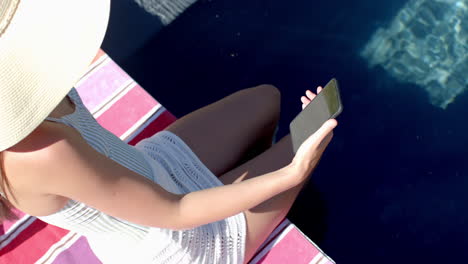 una adolescente caucásica está descansando junto a una piscina, usando su teléfono inteligente