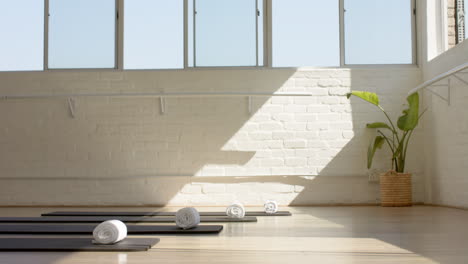 sunlight streams through large windows onto yoga mats and towels in bright studio