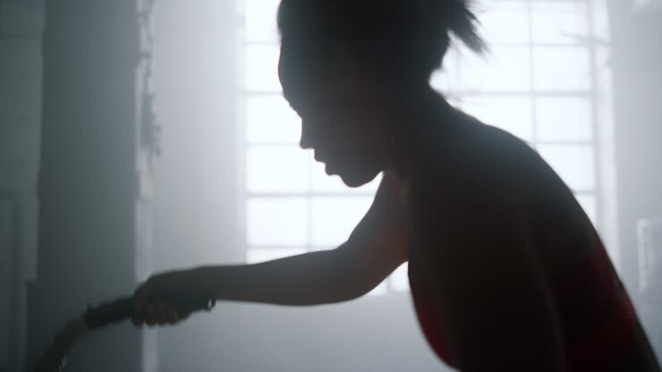 Donna energica che si allena con le battle ropes durante un allenamento di forza in palestra. Silhouette