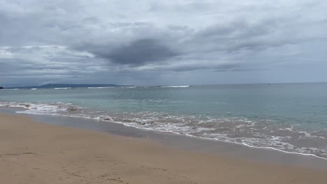 Overcast-sky-over-the-ocean,-waves-hitting-a-sandy-beach