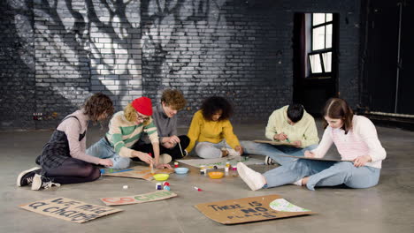 jóvenes activistas ambientales pintando carteles sentados en el suelo