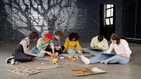 young environmental activists painting placards sitting on the floor