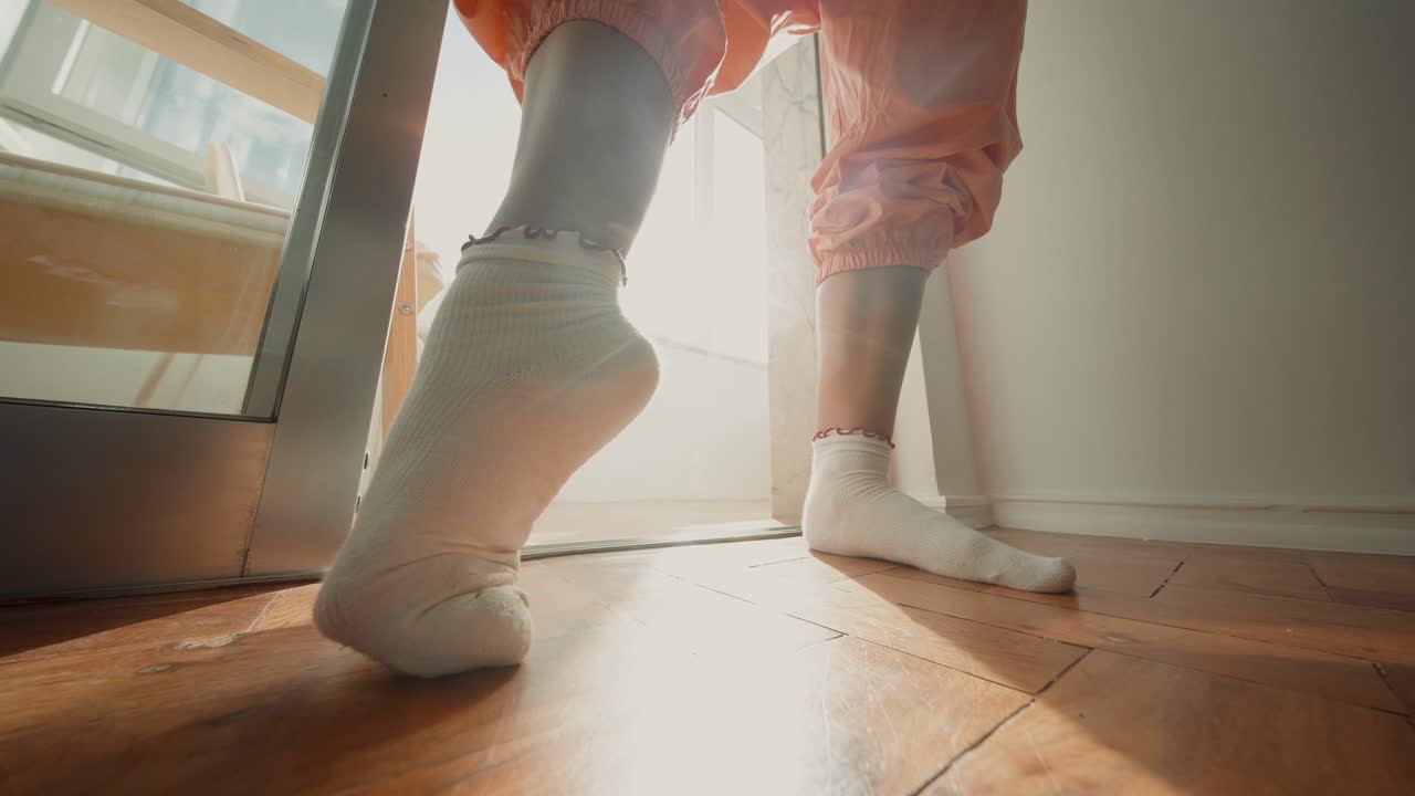 Person i strumpor och joggingbyxor som står på ett trägolv