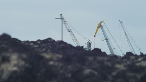 Grúas-Portuarias-Distantes-En-Un-Día-Nublado,-Puerto-De-Liepaja,-Montones-De-Algas-Muertas-En-Primer-Plano,-Tiro-Medio-De-ángulo-Bajo