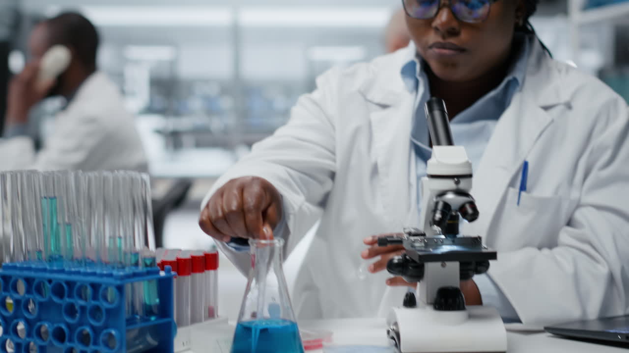 Technicien de laboratoire clinique pipetant un liquide bleu dans une éprouvette