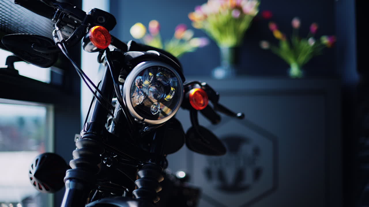A motorcycle standing in a room next to the window with tulips on the background