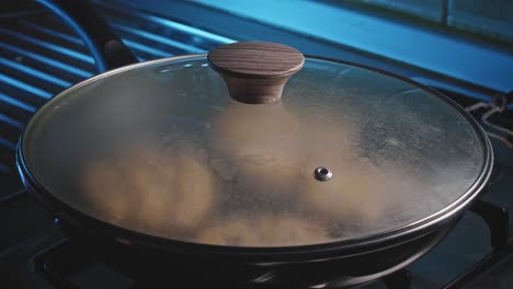 Cubriendo-A-Mano-Los-Buñuelos-En-Una-Sartén-Negra-Con-Una-Tapa-Transparente-De-Vidrio-En-Una-Estufa