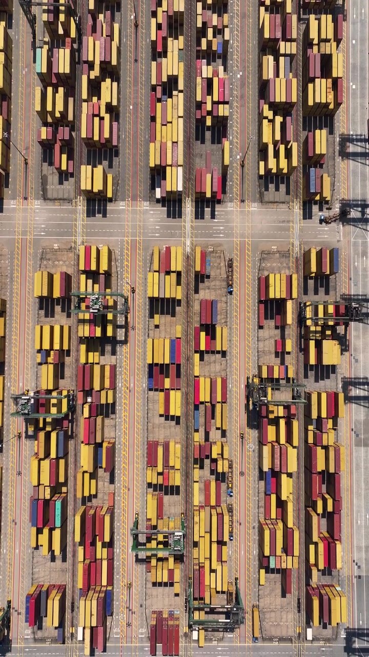A busy container terminal with numerous shipping containers arranged in rows. Cargo vehicles are moving between the containers, emphasizing freight transportation activity.