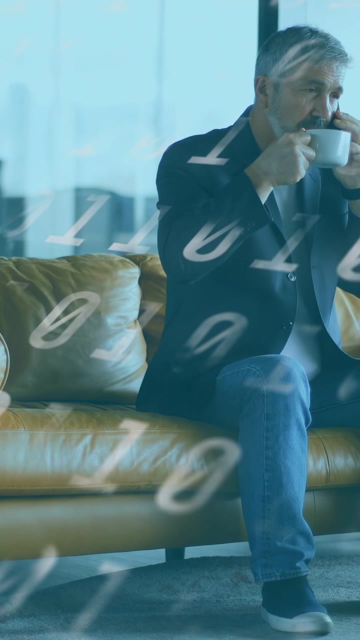 Vertical video: Man taking work call while sipping mug on sofa, binary digits drifting across frame