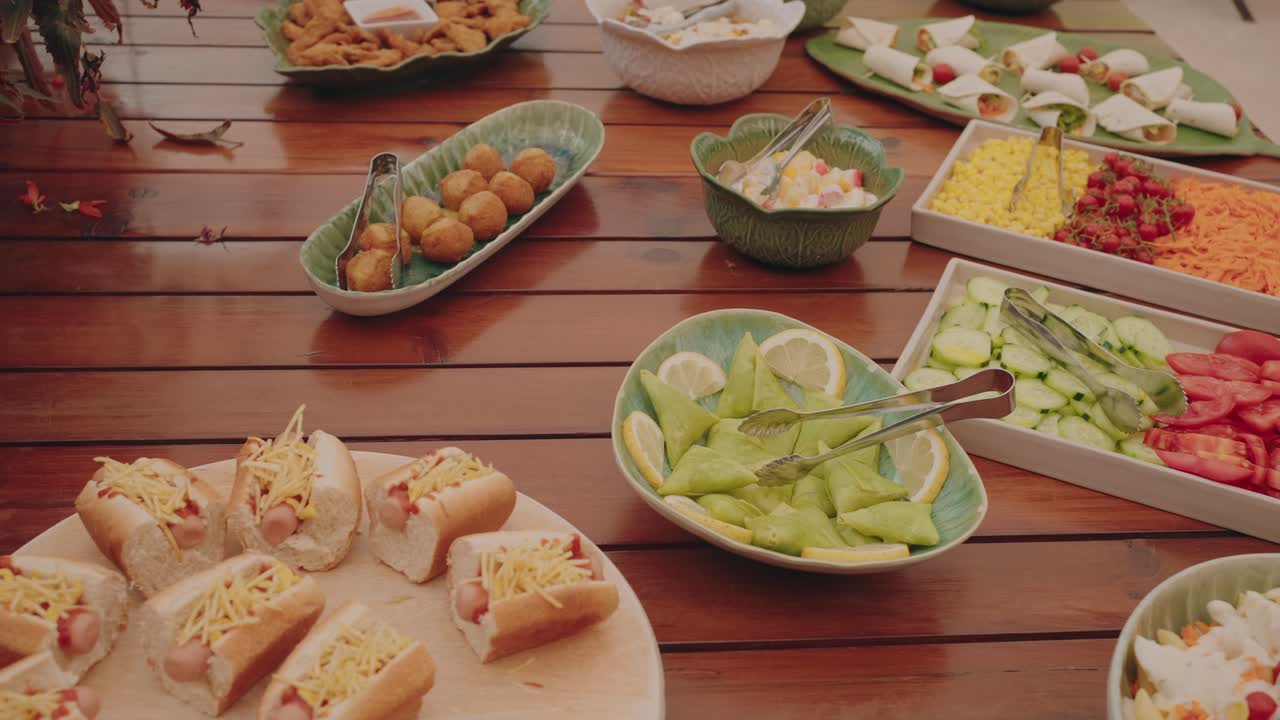 Buffet table with hot dogs salads fruits and appetizers displayed on wooden surface